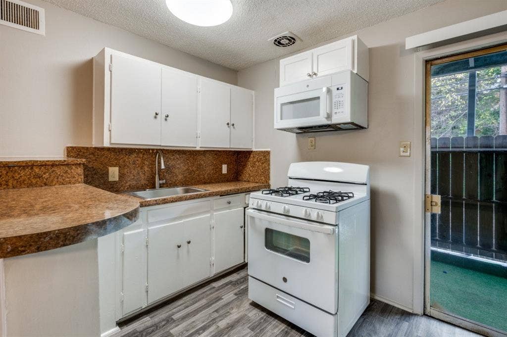 2213 Capri Drive, #208, Fort Worth, TX 76114 Kitchen featuring white cabinetry, brown granite-look countertops, stainless steel sink, wood-finish flooring, and a built-in microwave