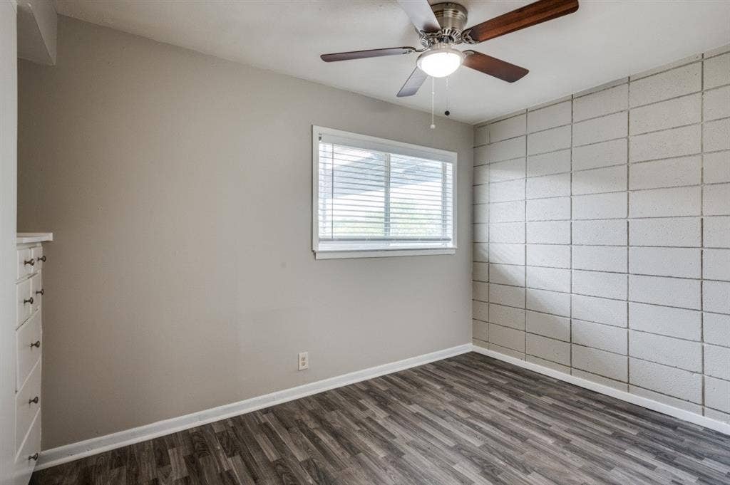 2213 Capri Drive, #208, Fort Worth, TX 76114 Wood-finish flooring, accent wall featuring rectangular paneling, window with horizontal blinds, built-in cabinetry with drawer pulls, and a ceiling fan with integrated lighting