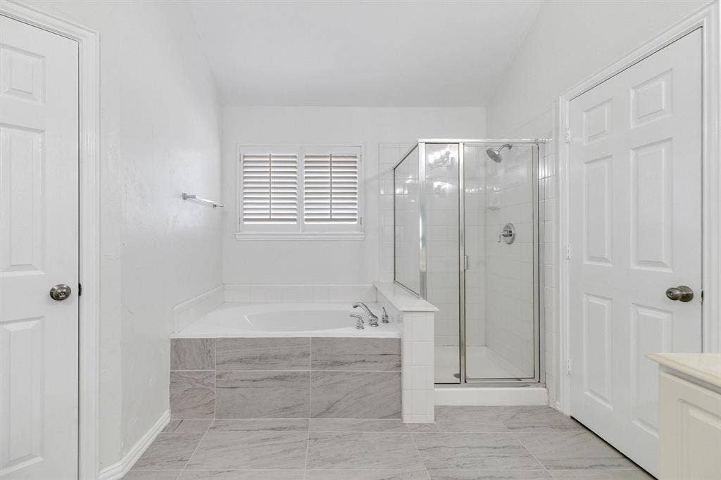 239 Glen Ridge Drive, Murphy, TX 75094 Built-in soaking tub with tile surround, glass-enclosed shower, louvered window, and light-toned tile flooring