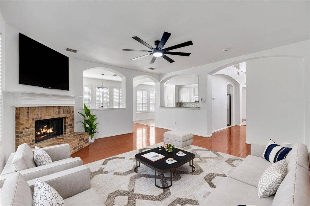 239 Glen Ridge Drive, Murphy, TX 75094 Brick fireplace with a substantial hearth, wood-finish flooring, recessed lighting, and arched architectural openings