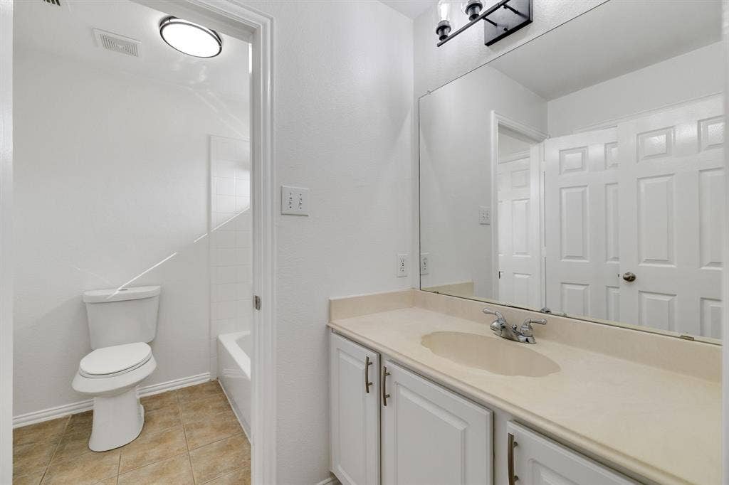 239 Glen Ridge Drive, Murphy, TX 75094 White vanity with cabinet storage, integrated sink, large wall-mounted mirror, and tile flooring