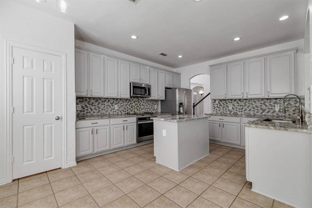 239 Glen Ridge Drive, Murphy, TX 75094 Kitchen featuring a central island, light-toned cabinetry, stainless steel appliances, patterned tile backsplash, and light-toned tile flooring