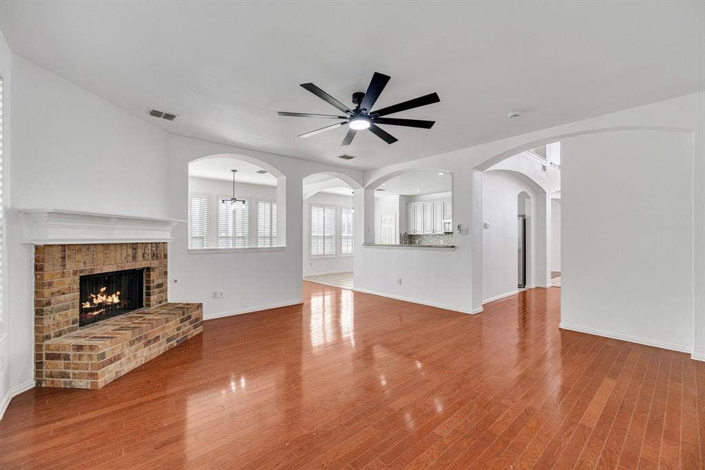 239 Glen Ridge Drive, Murphy, TX 75094 Wood-finish flooring, brick fireplace with mantel, arched doorways, white cabinetry, and a ceiling fan with integrated lighting