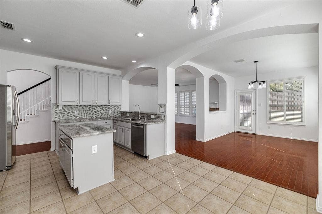 239 Glen Ridge Drive, Murphy, TX 75094 Kitchen featuring light gray cabinetry, stainless steel appliances, a mosaic tile backsplash, and a central island with a stone countertop