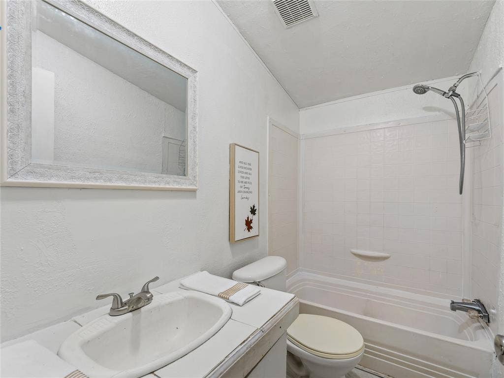 Clean and functional bathroom featuring a white porcelain sink with brushed nickel faucet, framed mirror with white finish, white subway tile walls, and an integrated shower-tub combination with chrome fixtures and glass enclosure panel