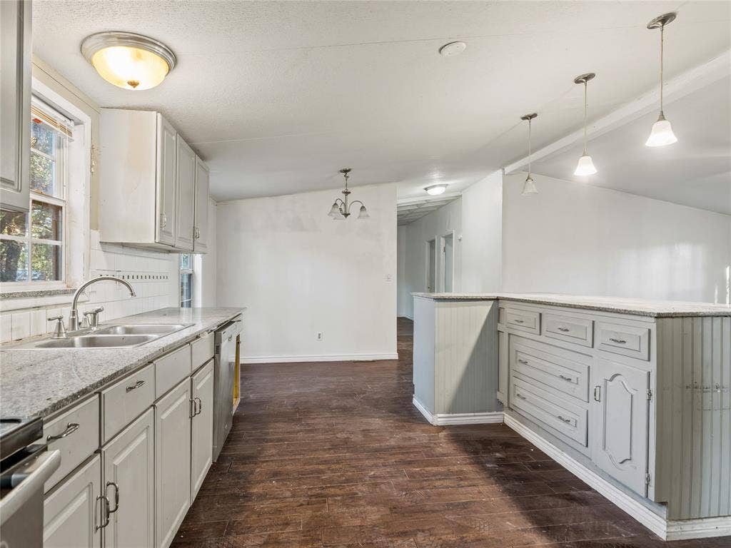 Kitchen featuring light-toned cabinetry, dual basin stainless steel sink, granite-style countertops, pendant lighting, and wood-finish flooring