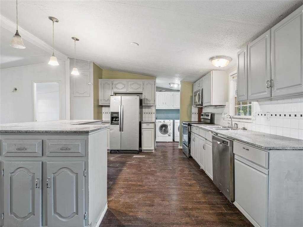 Kitchen featuring an island with a light-toned countertop, gray cabinetry, stainless steel appliances, and wood-finish flooring