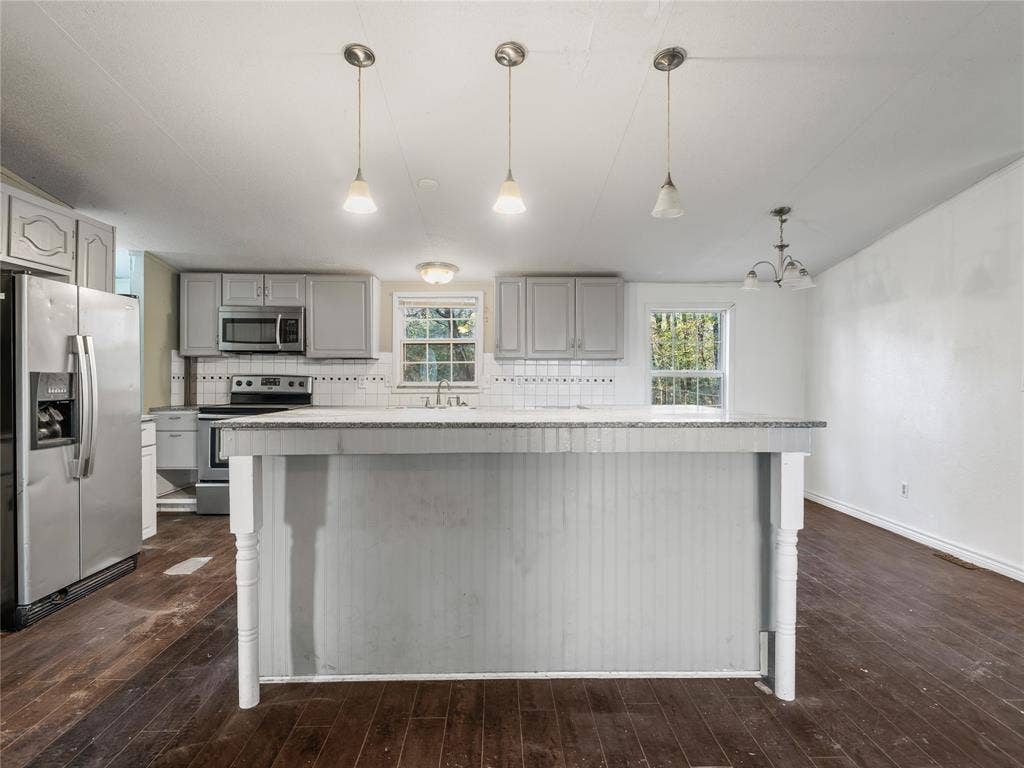 Kitchen featuring gray cabinetry, stainless steel appliances, white tile backsplash, a center island with beadboard detailing, and dark wood-finish flooring
