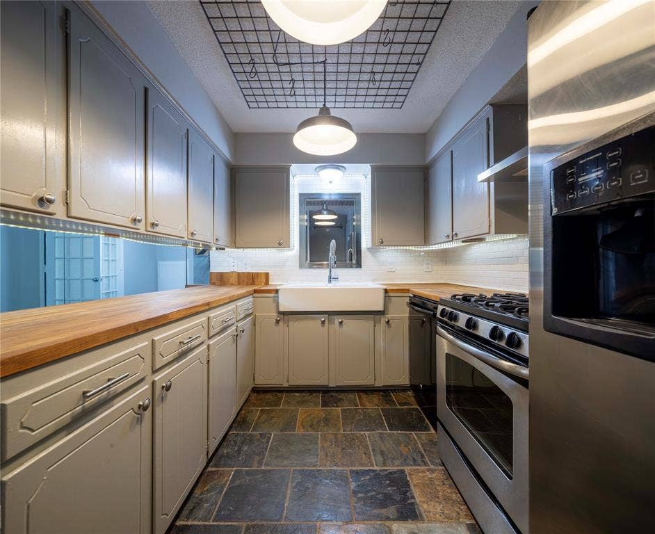 1717 N Locust Street, #1, Denton, TX 76201 Kitchen featuring slate-style flooring, light-colored cabinetry with modern hardware, wood-finish countertops, a white farmhouse-style sink, and stainless steel appliances
