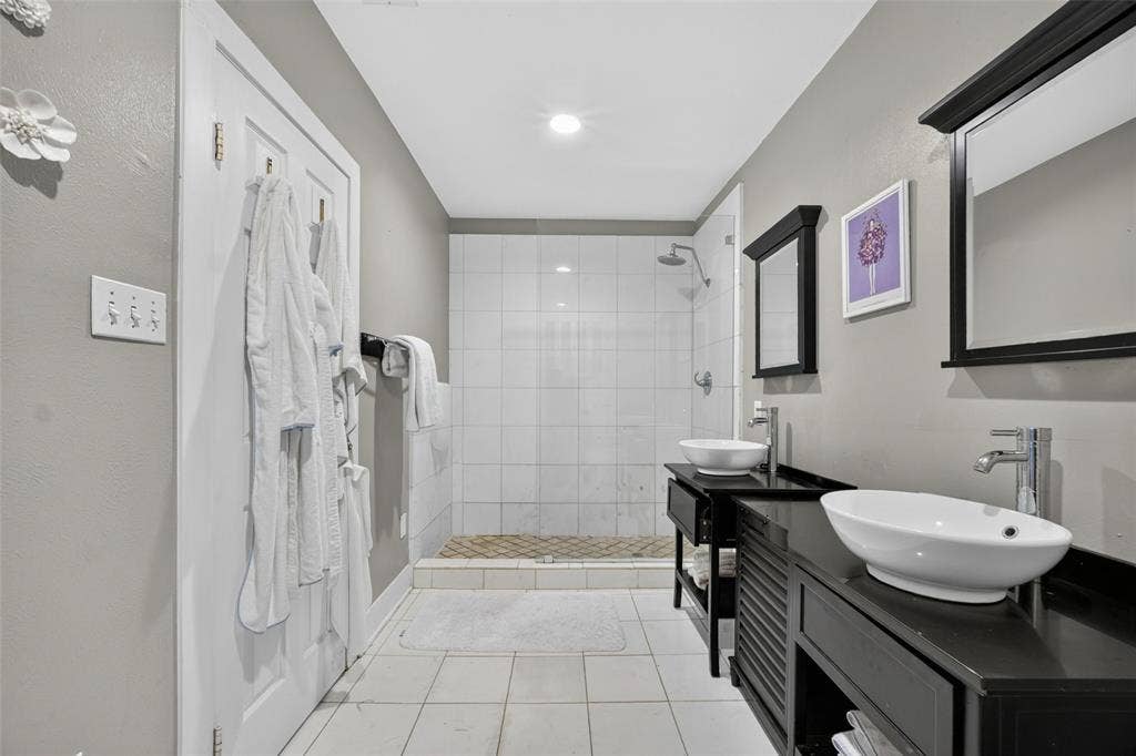 5630 Vanderbilt Avenue, Dallas, TX 75206 Spa-inspired primary bathroom featuring a walk-in shower with subway tile surround, dual vanities with vessel sinks and matte black hardware, recessed ceiling lighting, and neutral tile flooring throughout