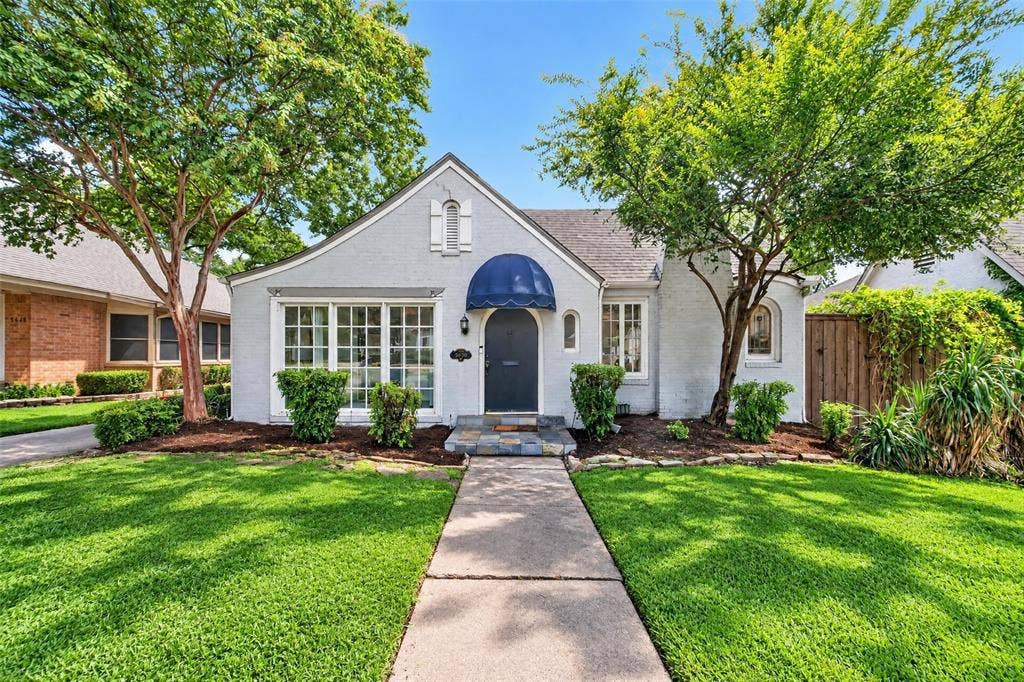 5630 Vanderbilt Avenue, Dallas, TX 75206 Gabled roofline with stucco exterior, multiple arched windows, prominent front entry with blue awning, and mature trees framing the property
