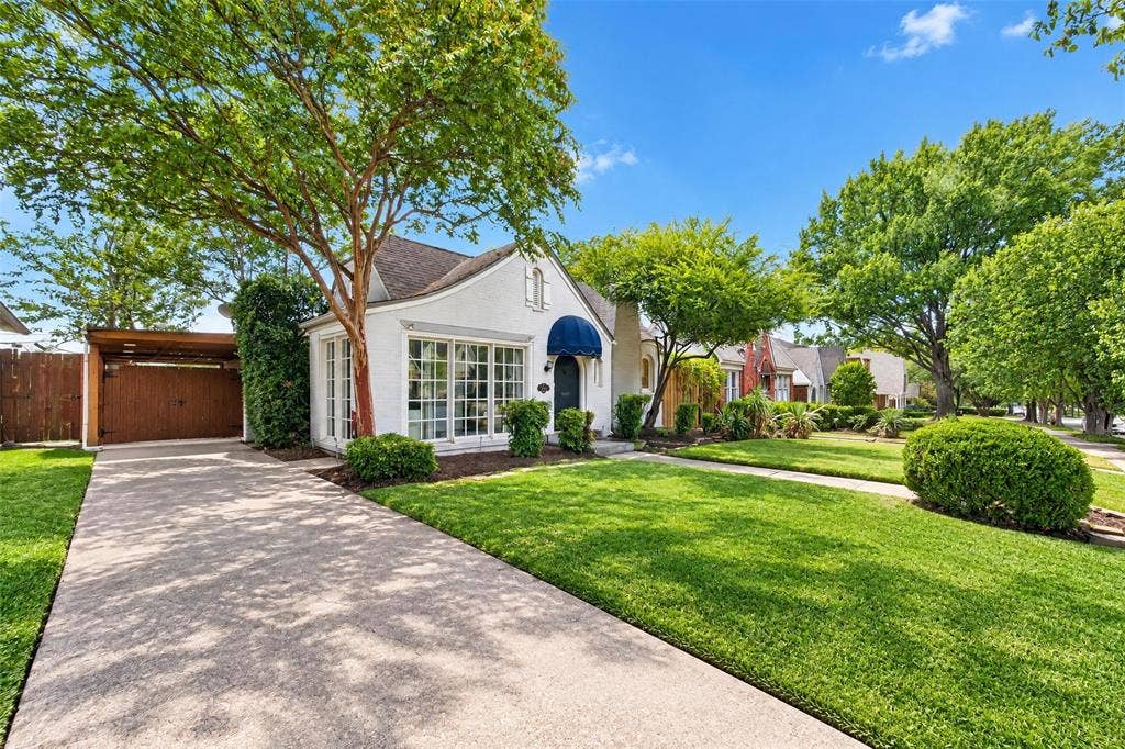 5630 Vanderbilt Avenue, Dallas, TX 75206 White stucco exterior with a blue awning, expansive front lawn, mature trees, and a concrete driveway leading to a covered carport