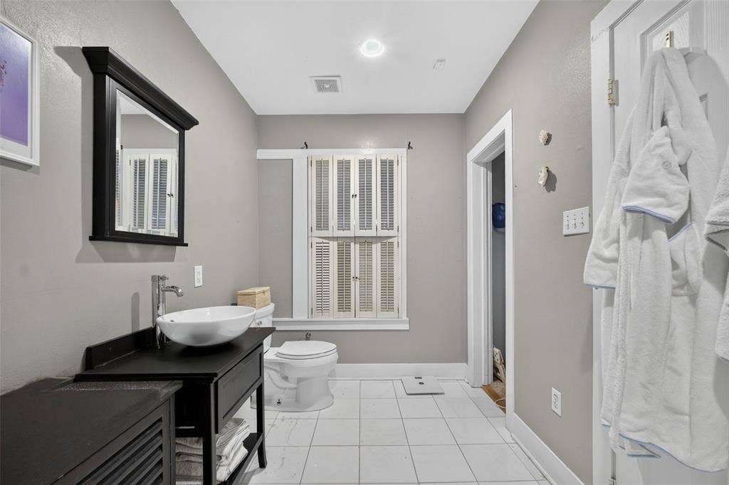 5630 Vanderbilt Avenue, Dallas, TX 75206 White vessel sink with chrome faucet, black vanity with open shelving, recessed lighting, and white tile flooring