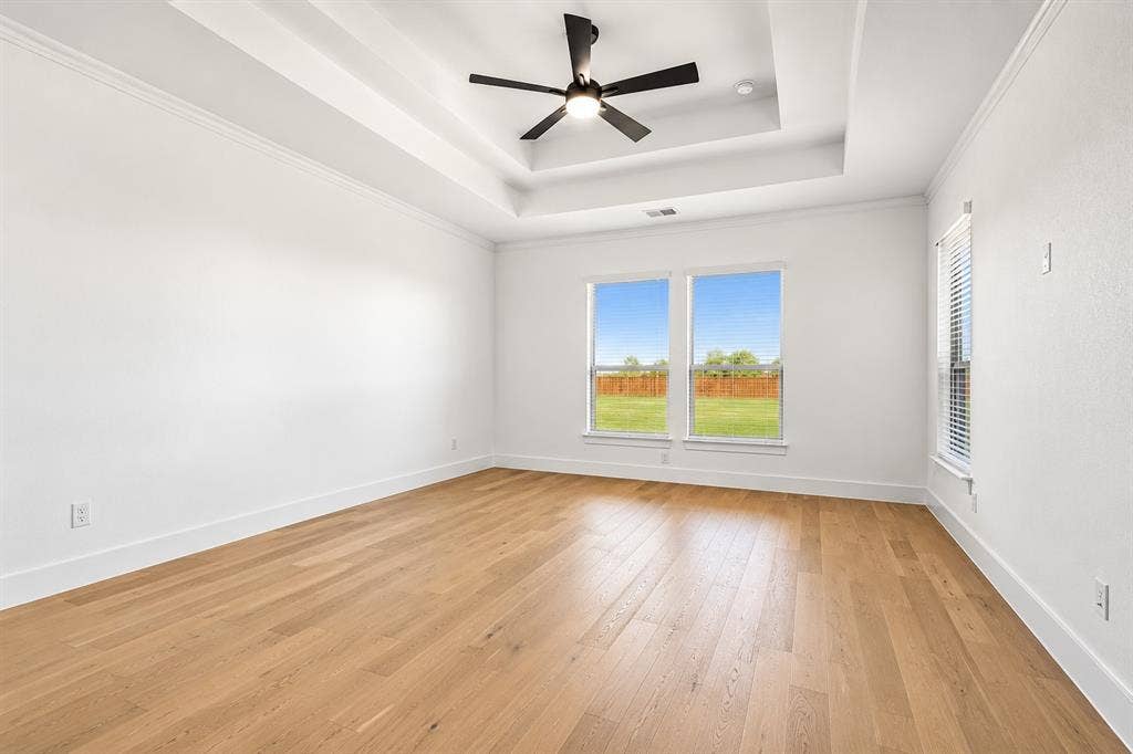 Primary Bedroom Tray ceiling with a central matte black ceiling fan, wood-finish flooring, and expansive windows