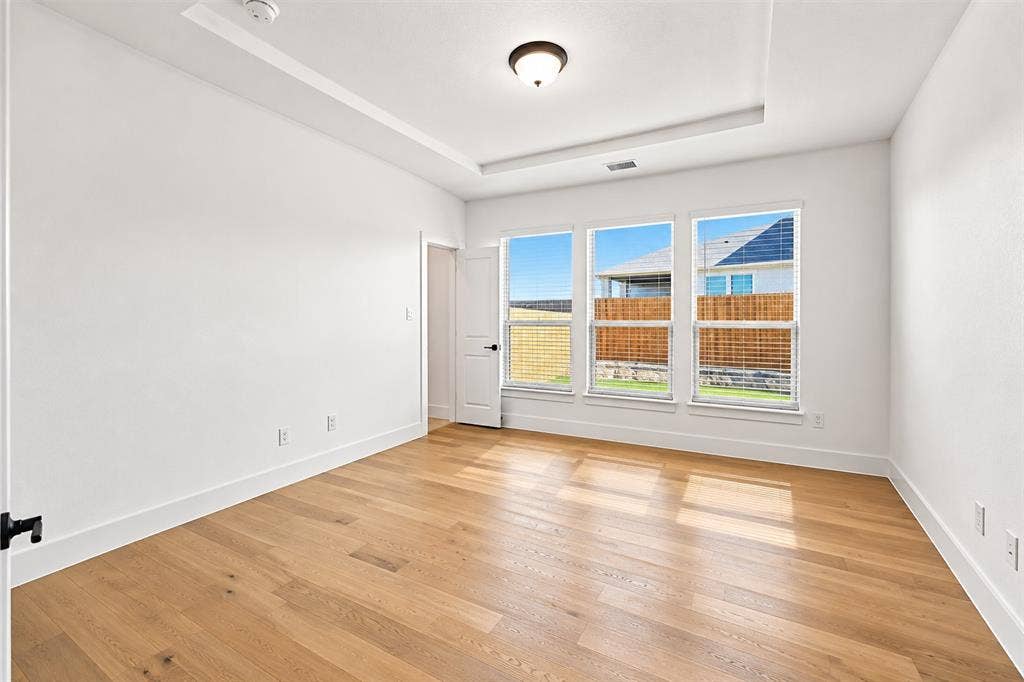 Office with tray ceiling with centered flush-mount lighting, wood-finish flooring, and three oversized windows providing natural light
