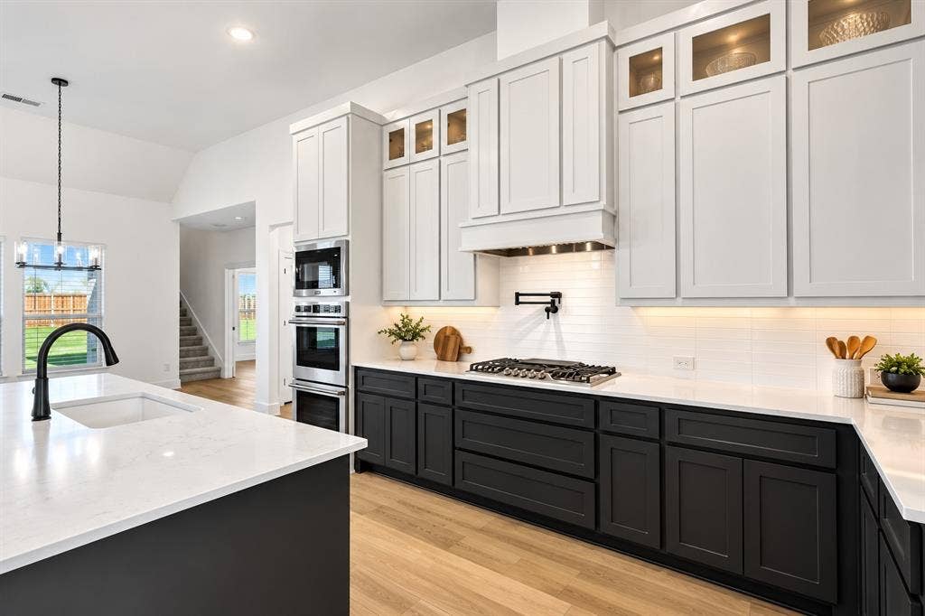 Kitchen featuring two-tone shaker cabinetry, quartz countertops, built-in stainless steel double ovens, a gas cooktop with a wall-mounted pot filler, and wood-finish flooring