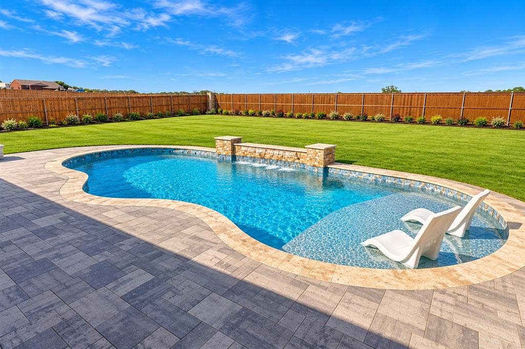 Curved swimming pool with an integrated sun shelf, stone water feature, and paver decking