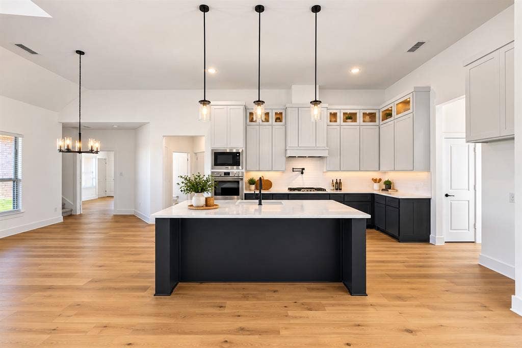 Kitchen featuring a large center island with a white countertop, two-toned cabinetry, built-in stainless steel appliances, and pendant lighting