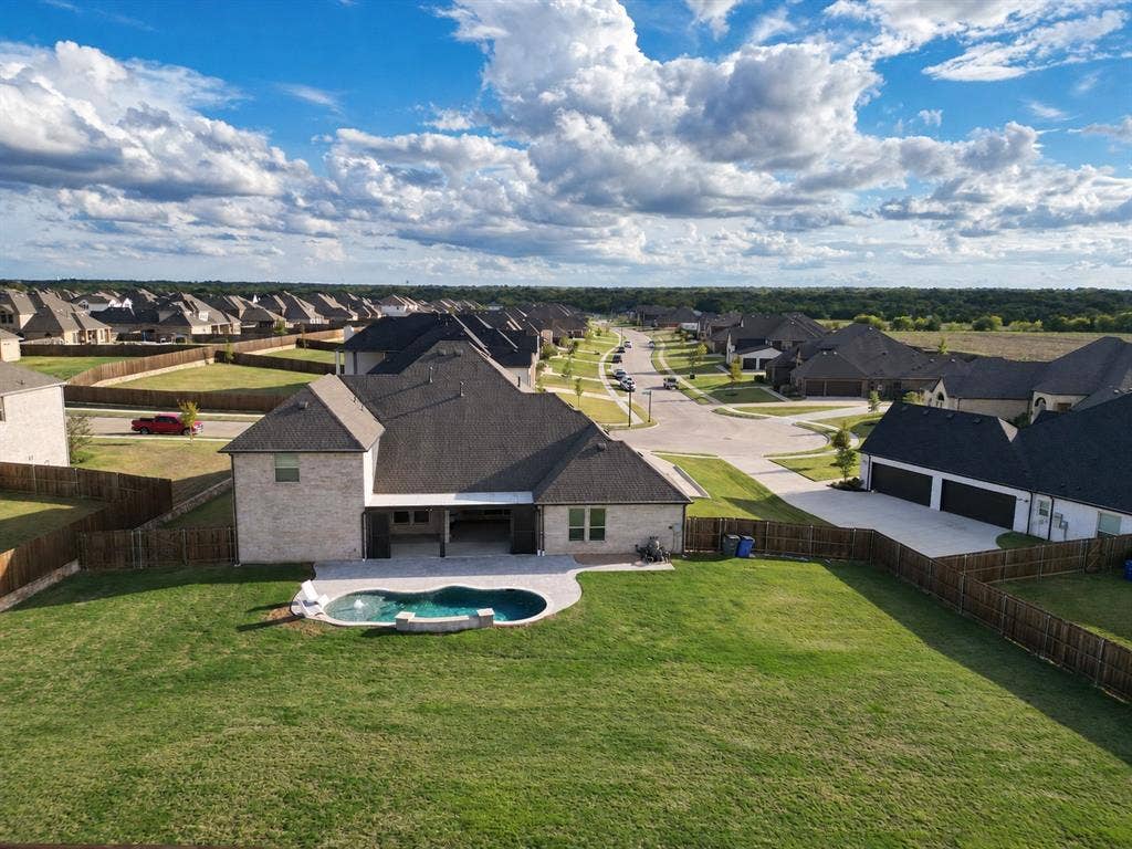 Aerial perspective of a brick exterior residence featuring a covered patio, a custom-shaped swimming pool with stone surround, and a fenced backyard