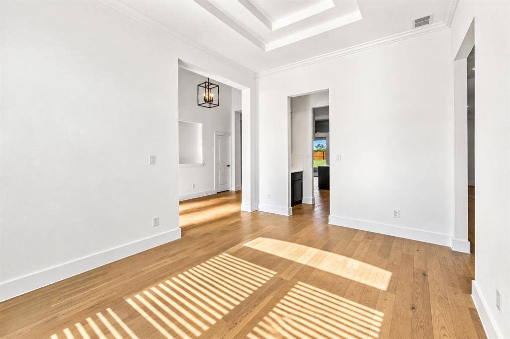 Formal Dining Room Interior space featuring wood-finish flooring, a tiered tray ceiling, crown molding, and a four-light geometric pendant fixture