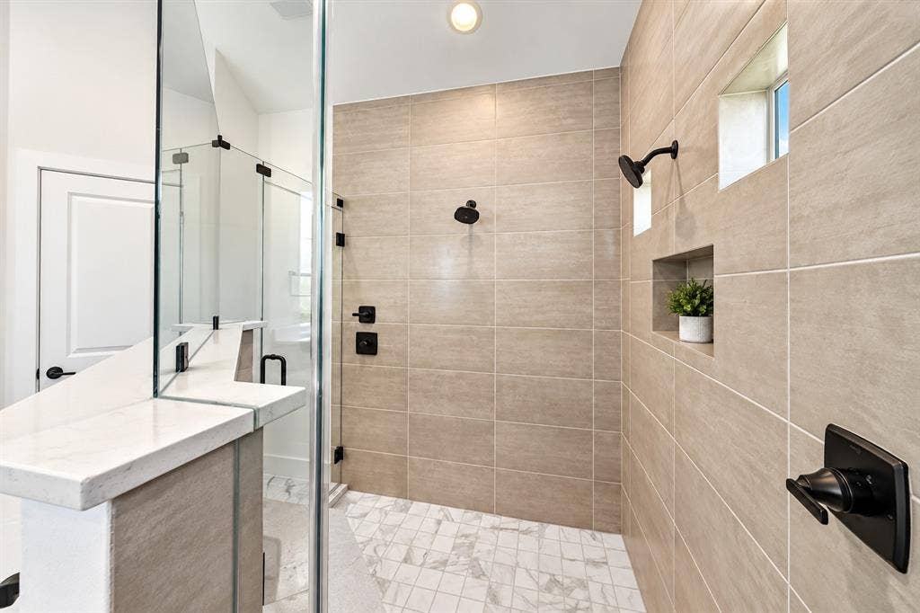 Walk-in shower featuring large-format neutral tile walls, matte black plumbing fixtures, built-in tile shelving, and glass enclosure panels