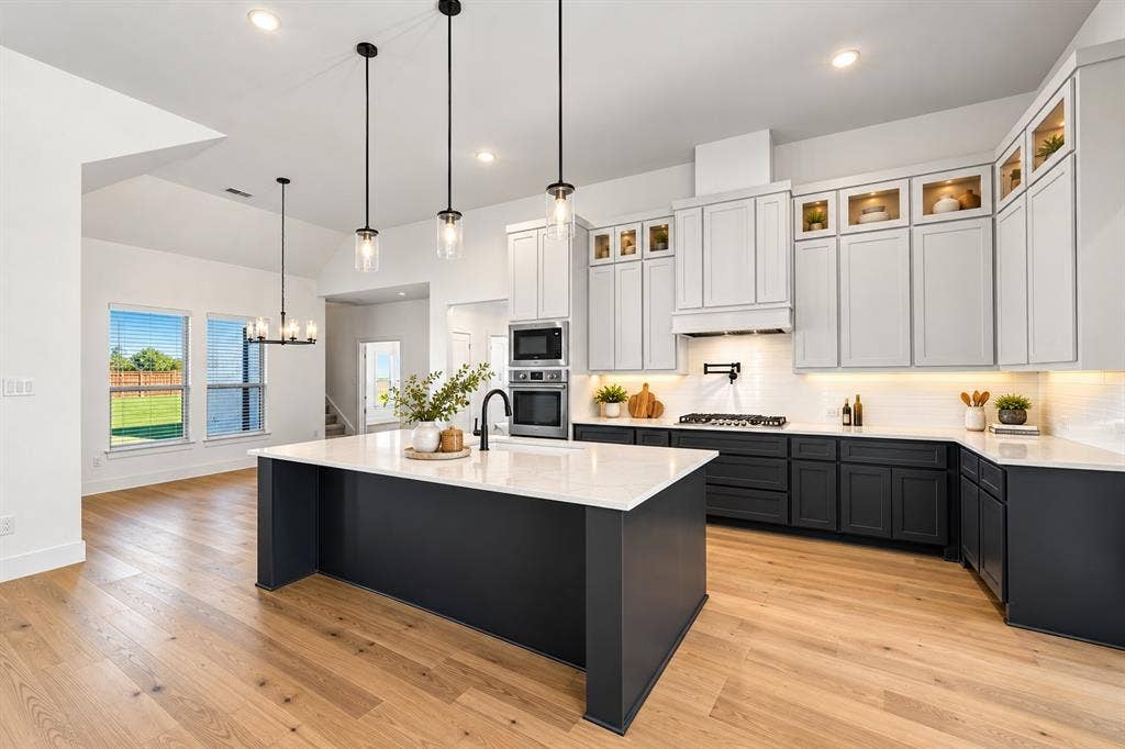 Kitchen featuring two-tone shaker cabinetry, quartz countertops, a central island with a matte black faucet, stainless steel built-in double wall ovens, and wood-finish flooring