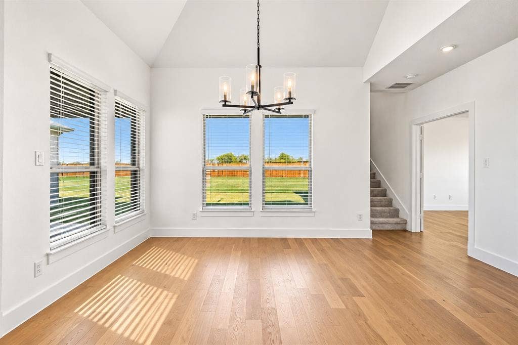 In Kitchen Dining Area with Vaulted ceilings, wood-finish flooring, multi-pane windows, and a central five-light chandelier