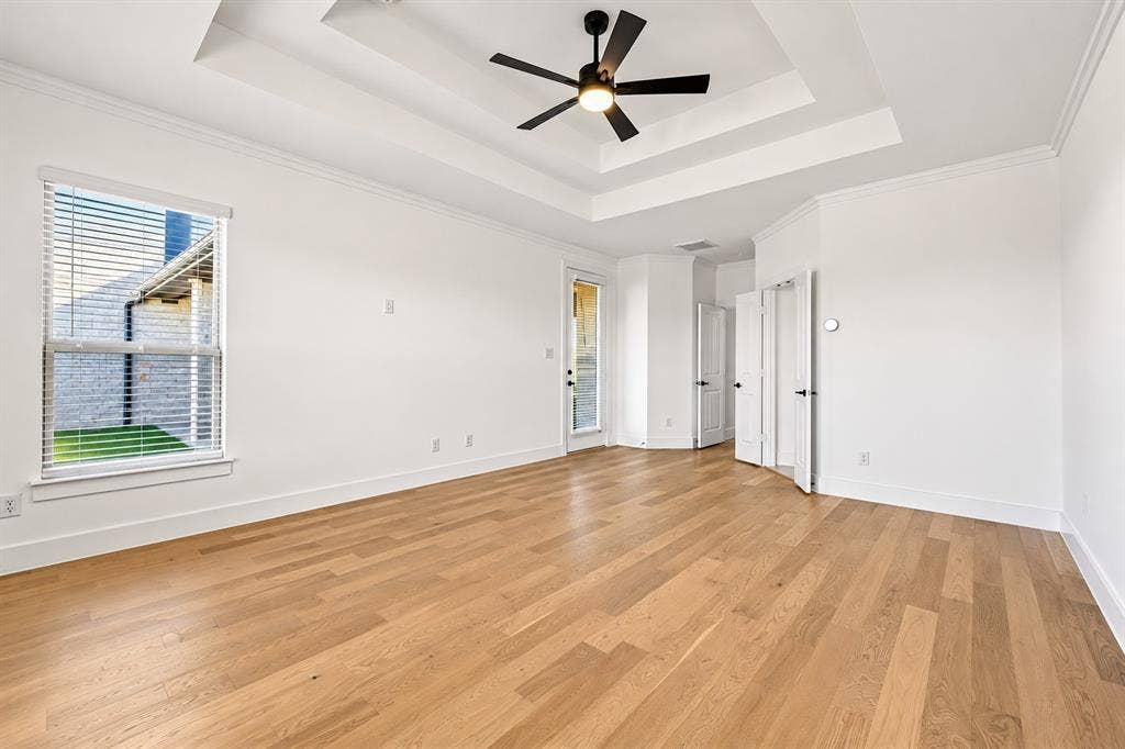 Primary Bedroom Tray ceiling with a matte black ceiling fan, wood-finish flooring, and crisp white wall finishes