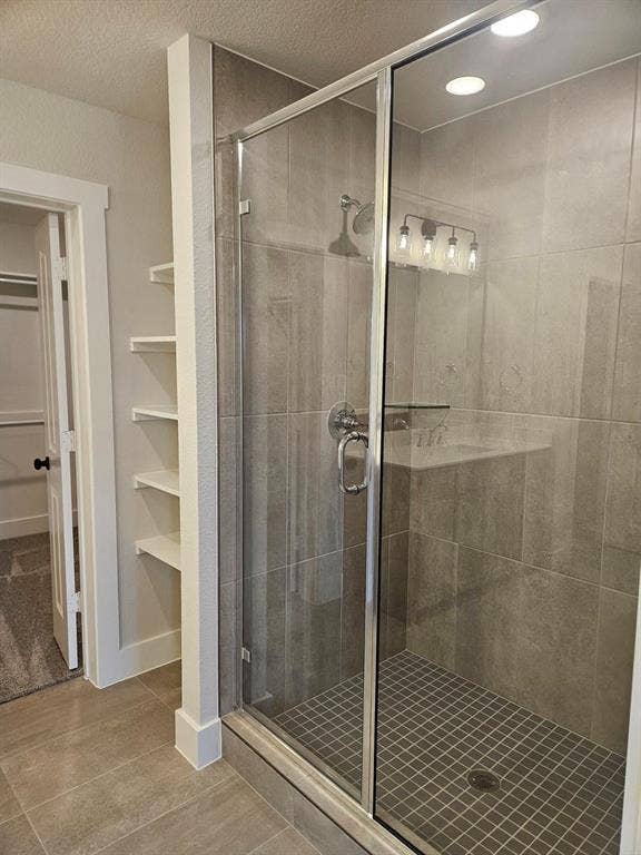 221 Chestnut Street, Celina, TX 75009 Frameless glass shower enclosure with a rainfall showerhead, recessed lighting, and wall-mounted shelving