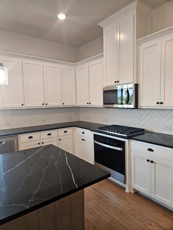 221 Chestnut Street, Celina, TX 75009 White shaker cabinetry, dark countertops with light veining, stainless steel appliances, herringbone tile backsplash, and wood-finish flooring