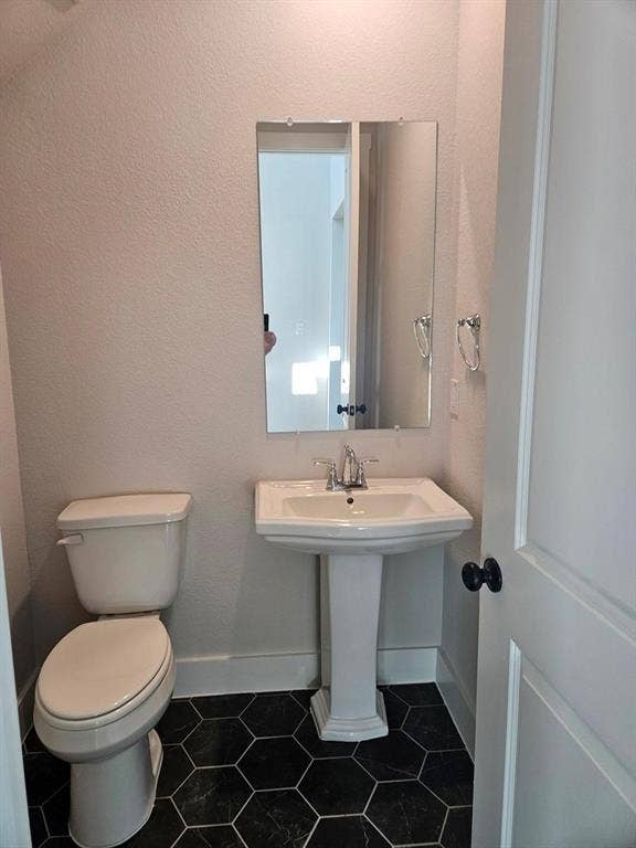 221 Chestnut Street, Celina, TX 75009 Pedestal sink with chrome faucet, wall-mounted mirror, white toilet, and dark hexagonal floor tiles