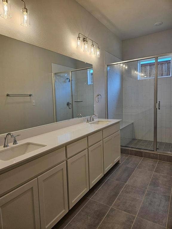 221 Chestnut Street, Celina, TX 75009 Dual vanity with integrated sinks, brushed nickel fixtures, a frameless glass shower enclosure, a built-in shower bench, and large format floor tiling