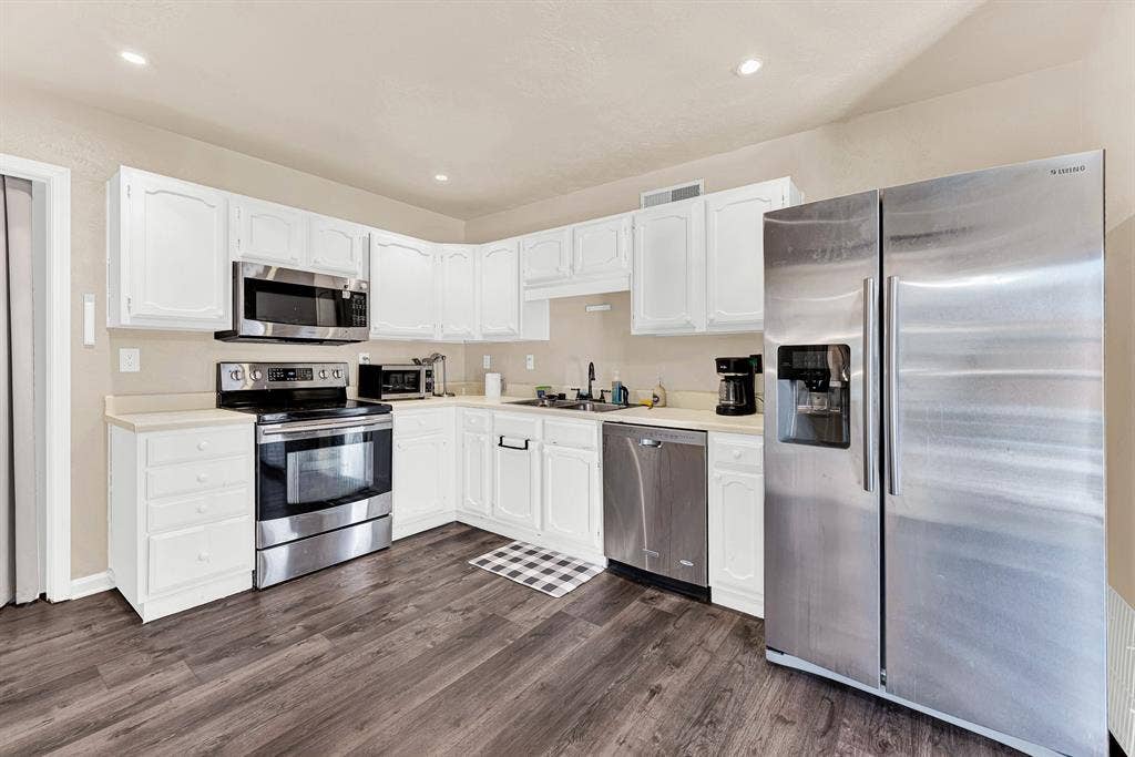 108 Kingsbridge Drive, Garland, TX 75040 Kitchen featuring stainless steel appliances, white cabinetry, light-toned countertops, and wood-finish flooring