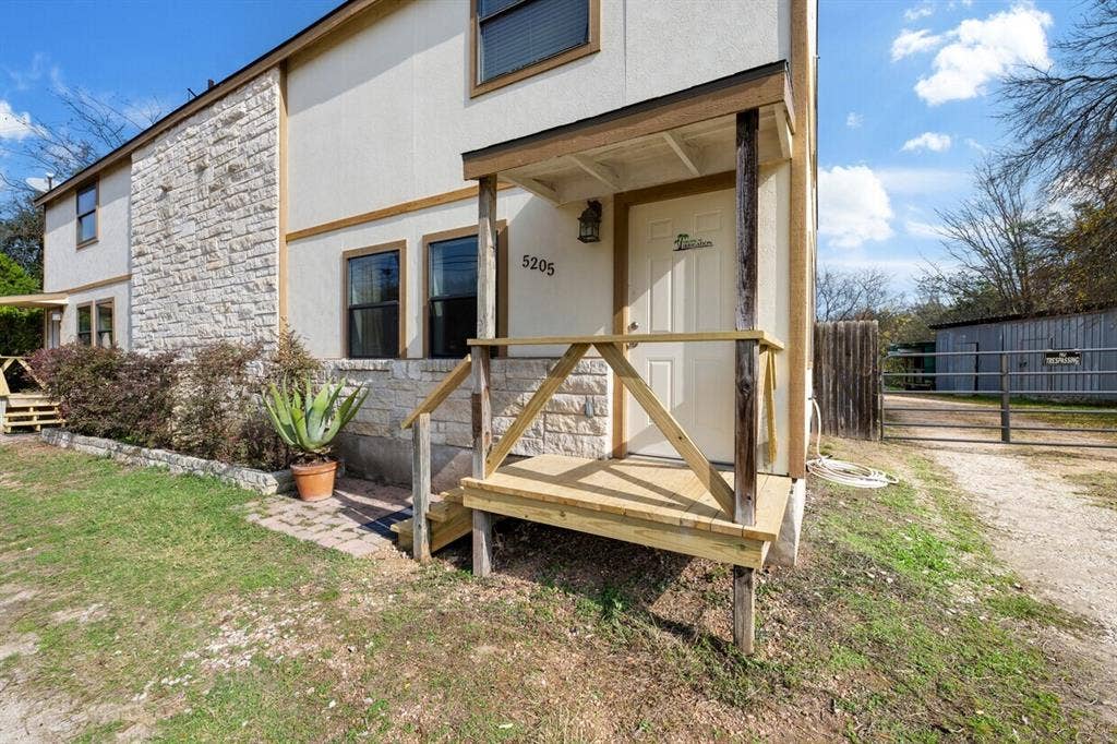 5205 Hudson Bend Road, Austin, TX 78734 Stucco and stone facade with multiple windows, featuring a covered front entry porch with wood railing and steps