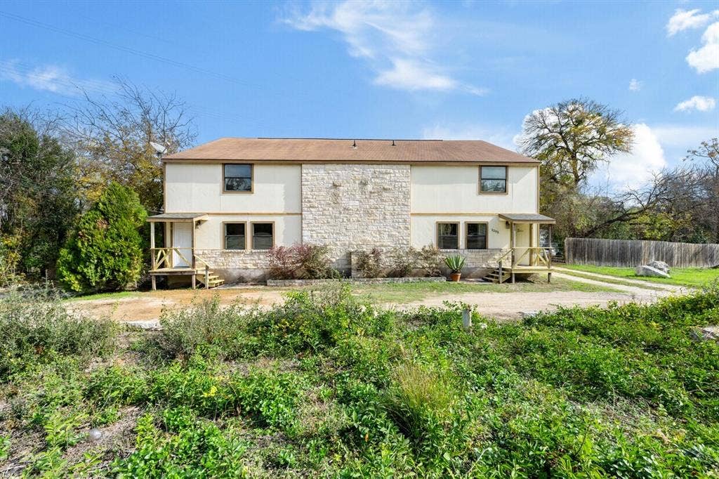 5205 Hudson Bend Road, Austin, TX 78734 Two-story exterior with stone and stucco facade, two covered entry porches with wood railings, and a partial privacy fence