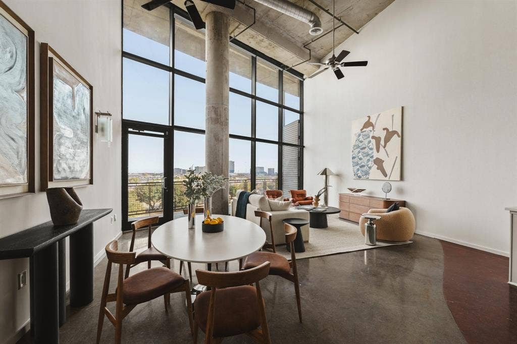 Polished concrete flooring, exposed concrete ceiling, industrial-style ceiling fan, full-height window wall with dark framing, and a concrete structural column