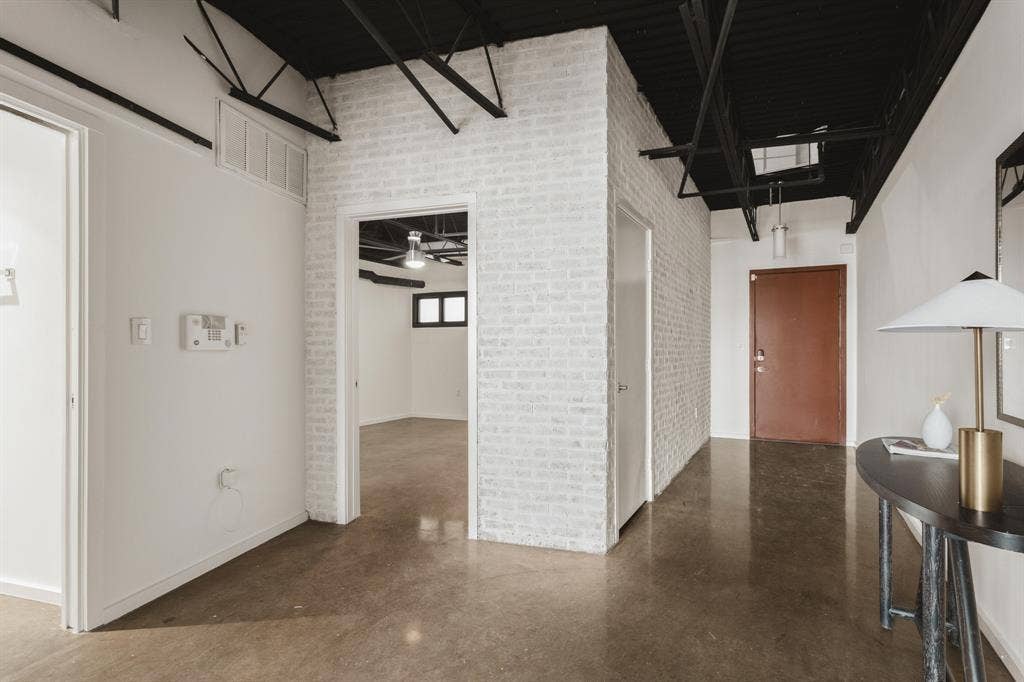 Polished concrete flooring, white painted brick accent wall, exposed black ceiling joists, recessed ceiling lighting, and a solid core entry door
