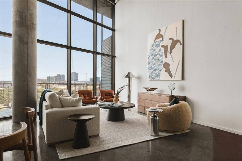 Expansive floor-to-ceiling windows, exposed concrete column, polished concrete flooring, white walls, and a light-toned area rug
