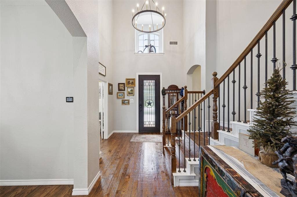 1000 Fenwick Lane, Forney, TX 75126 Soaring ceilings with a large chandelier, wood-finish flooring, and a staircase with dark wood handrails and wrought iron balusters
