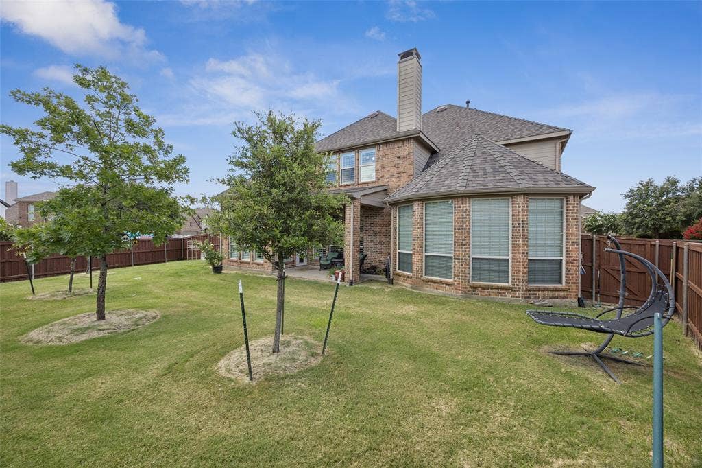 1000 Fenwick Lane, Forney, TX 75126 Expansive grassy yard with young trees, brick exterior, multiple windows, and a wood privacy fence