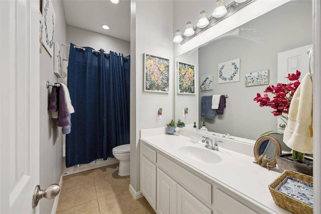 1000 Fenwick Lane, Forney, TX 75126 Vanity with integrated sink and chrome faucet, large vanity mirror, recessed ceiling lighting, tile flooring, and a white toilet