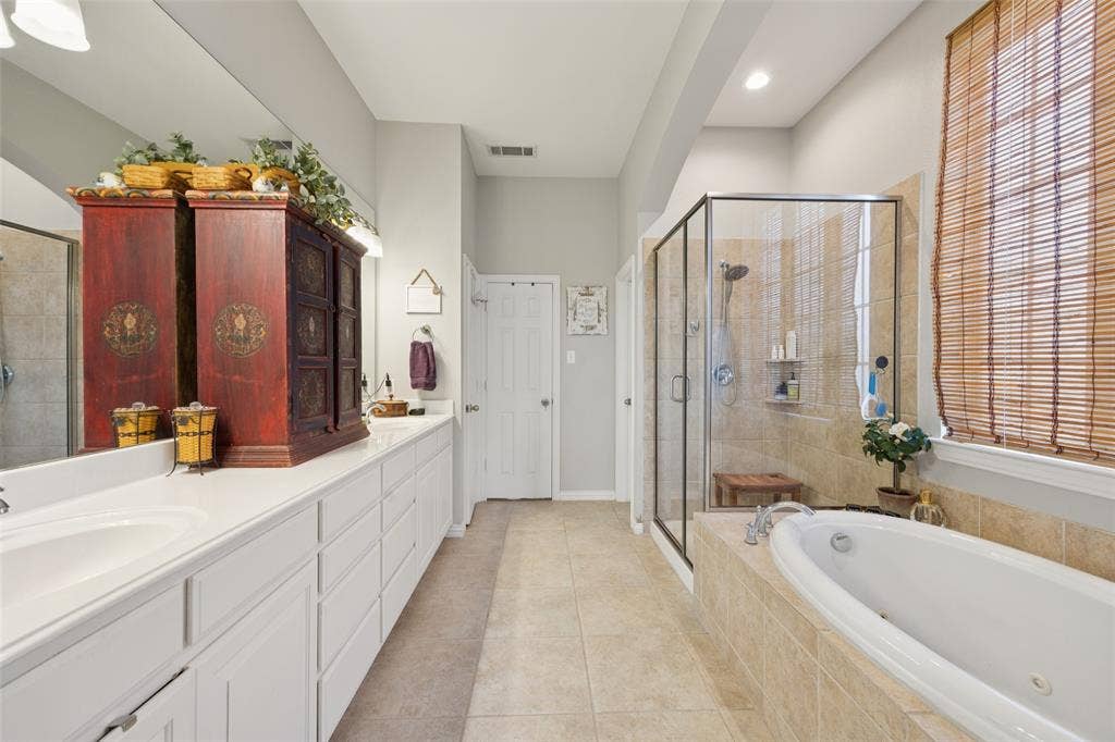 1000 Fenwick Lane, Forney, TX 75126 Dual vanity with extensive white cabinetry, large built-in soaking tub, separate glass-enclosed shower, and tiled flooring