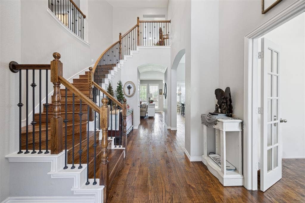 1000 Fenwick Lane, Forney, TX 75126 Expansive entryway featuring wood-finish flooring, a grand curved staircase with dark wood handrails, wrought iron balusters, and an arched doorway