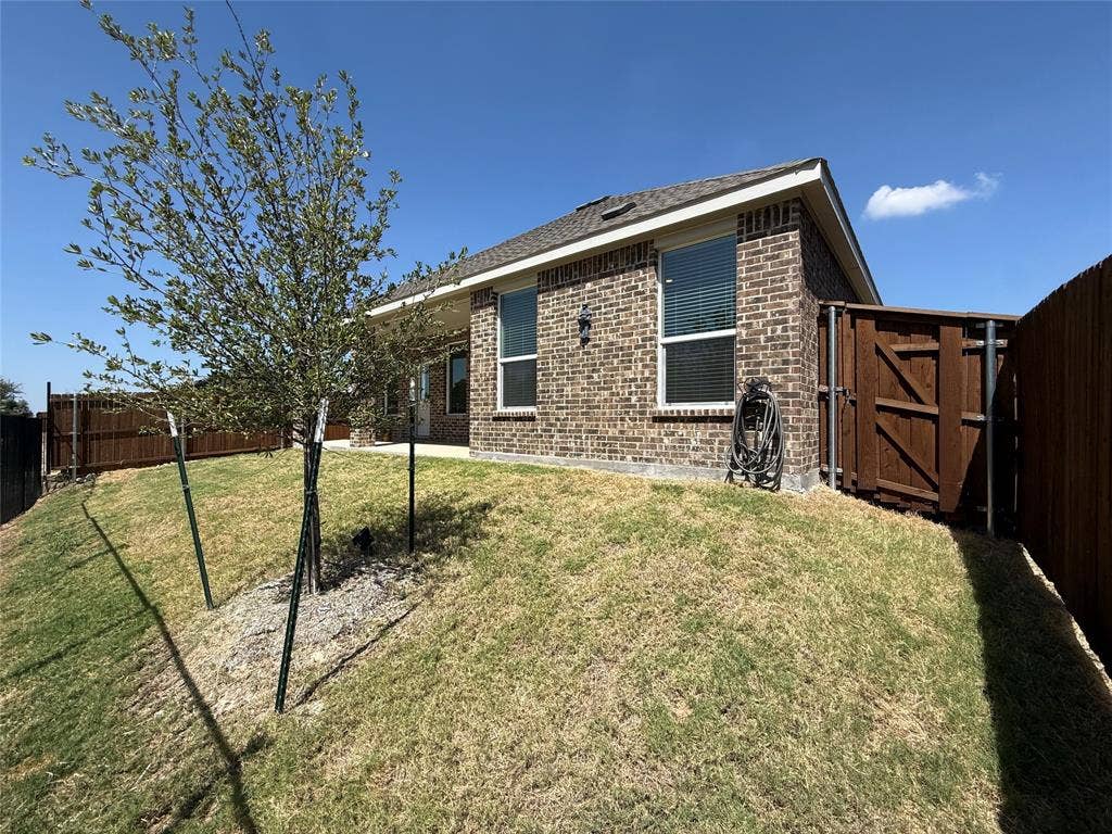 Brick exterior featuring a hip roof, privacy fencing, and a side gate