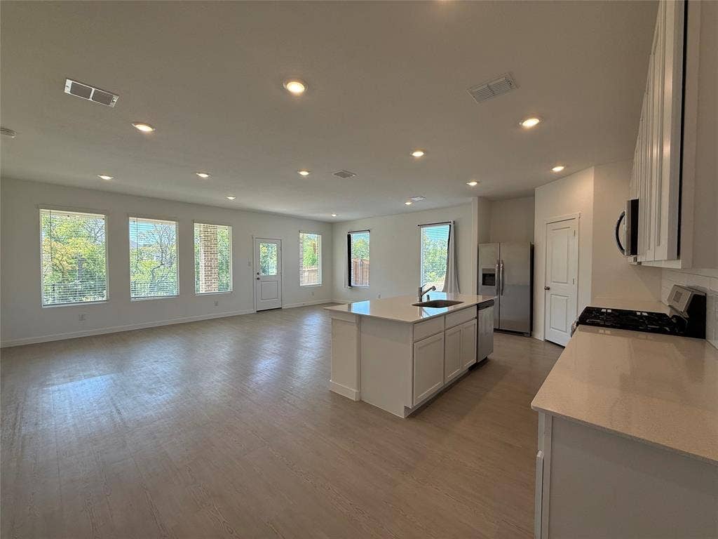Open-concept kitchen and living area featuring wood-finish flooring, recessed lighting, and ample natural light from multiple windows