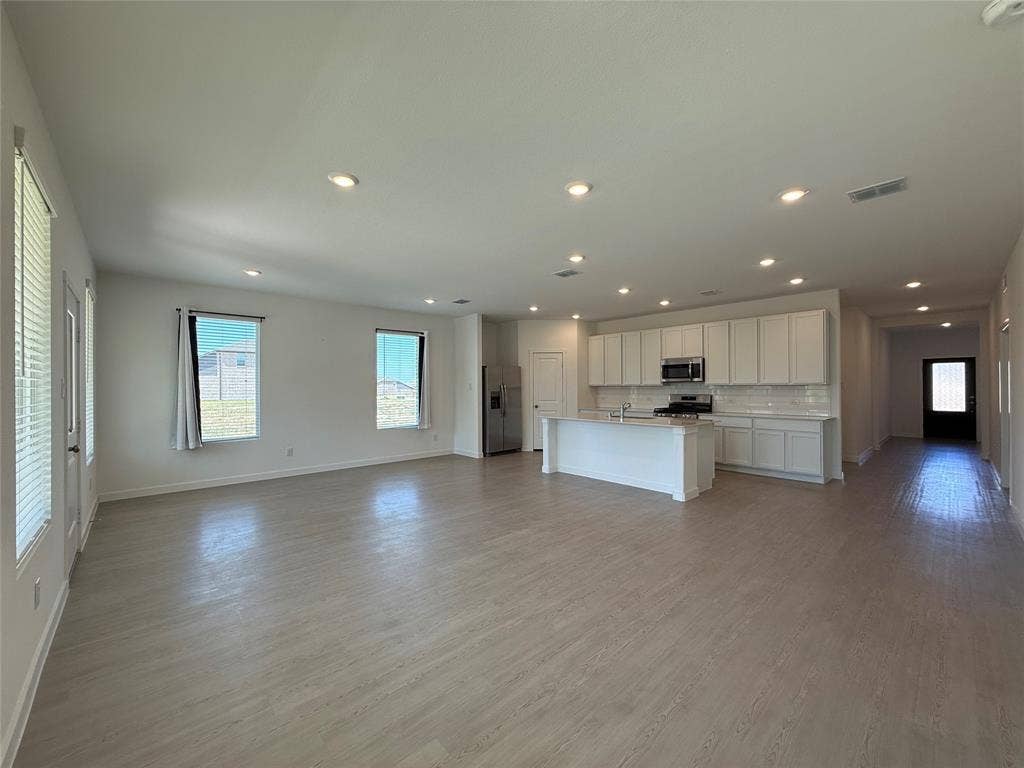 Open-concept living space featuring wood-finish flooring, recessed lighting, and a kitchen with white cabinetry, a center island, and stainless steel appliances