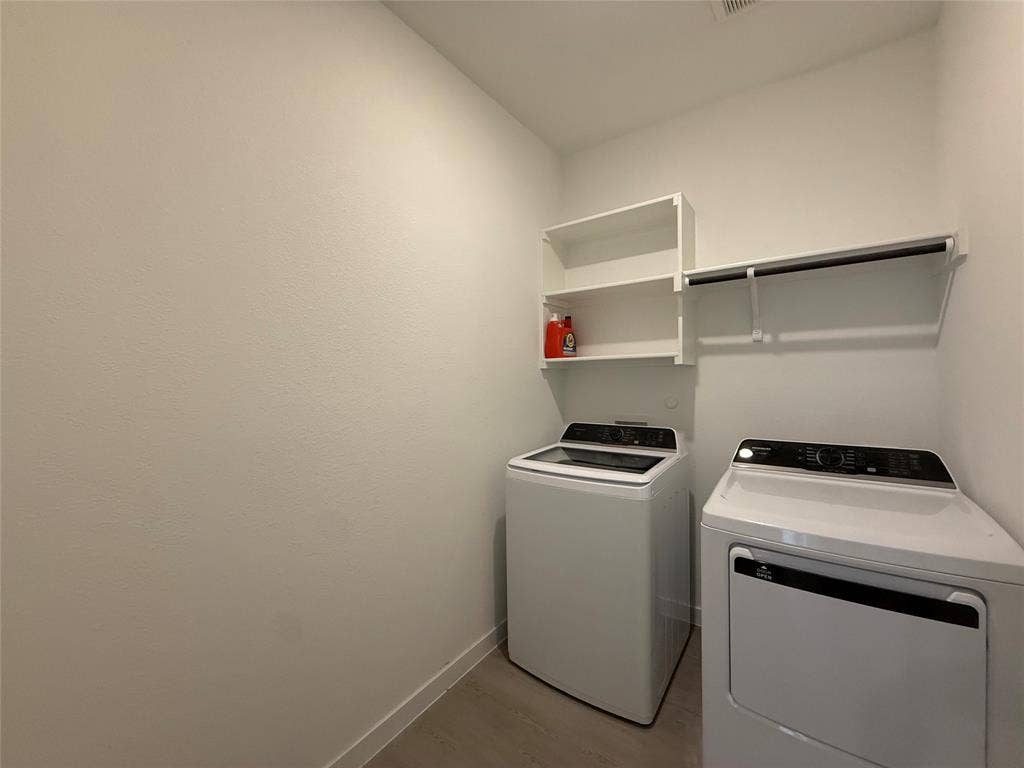Dedicated laundry area featuring built-in white shelving, a clothing rod, and wood-finish flooring