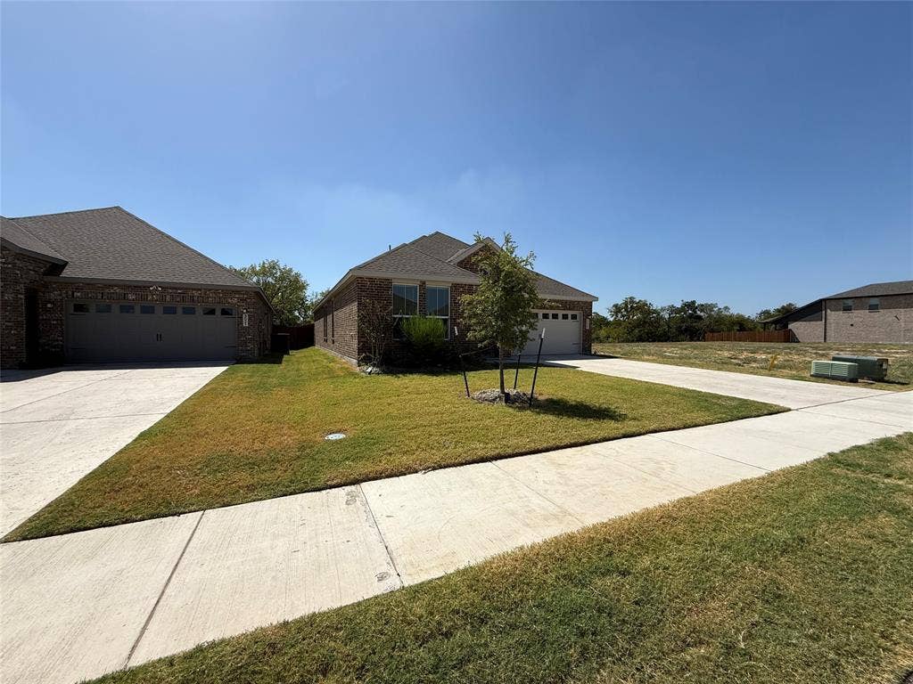 Brick exterior with an attached two-car garage, concrete driveway, and a front yard with established landscaping