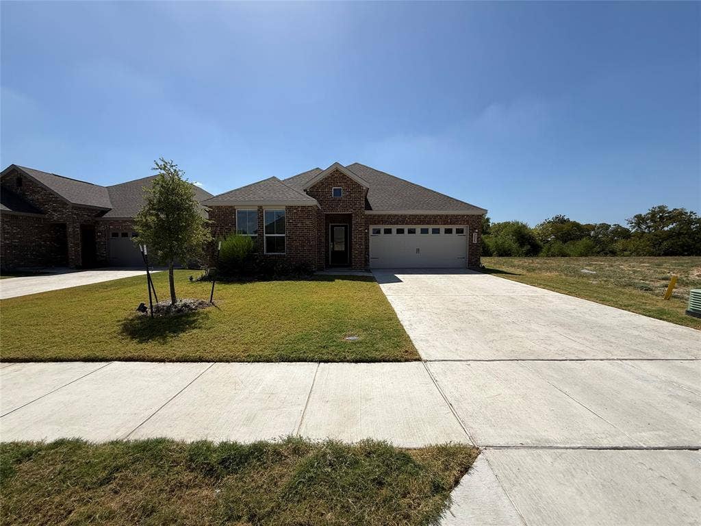 Brick exterior with an attached garage, paved driveway, and established front yard landscaping