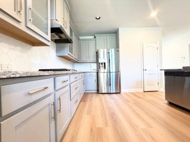 5609 Meritage Street, McKinney, TX 75070 Light wood-finish flooring, light gray cabinetry with brushed nickel hardware, stainless steel appliances, speckled stone countertops, and a white hexagonal tile backsplash